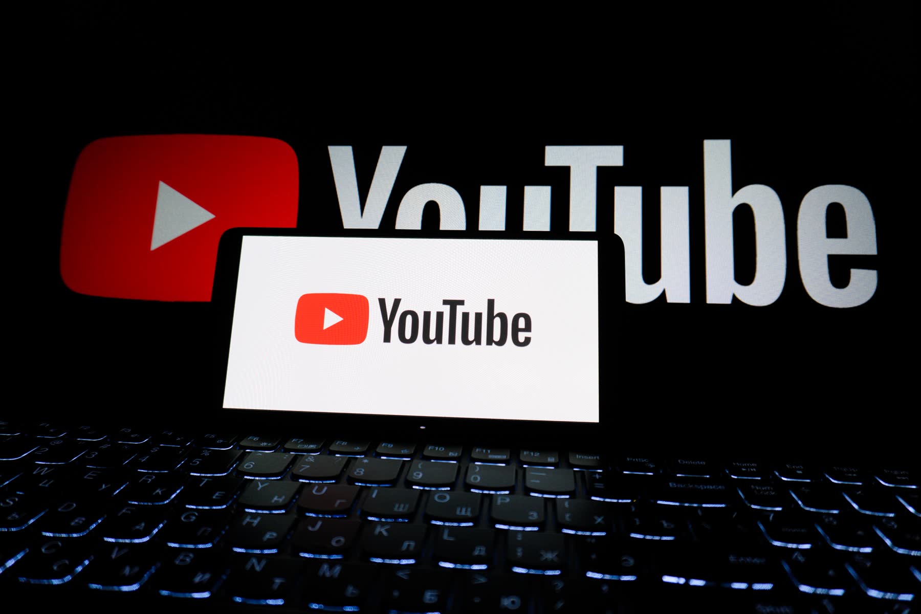 YouTube logo on a phone and laptop in a dark room